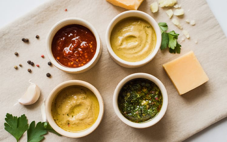 Molhos feitos em casa em potes de vidro sobre mesa rústica com ingredientes frescos em volta