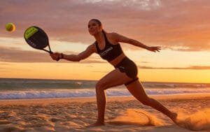 Jogadora de beach tennis queimando calorias em partida ao ar livre, em cenário ensolarado.