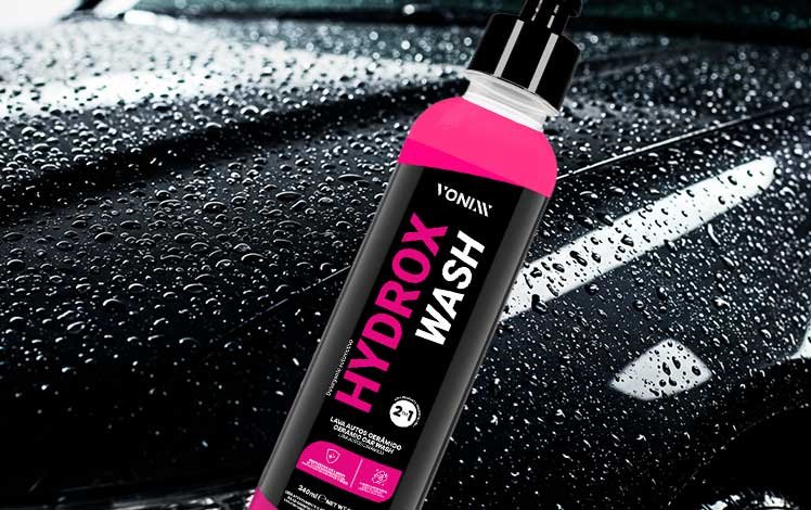 Carro preto sendo lavado com shampoo cerâmico Hydrox Wash, espuma cobrindo a lataria e brilho refletido na pintura.