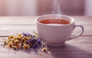 Xícara de chá de camomila e lavanda com vapor subindo sobre mesa de madeira clara, representando calma e bem-estar natural.