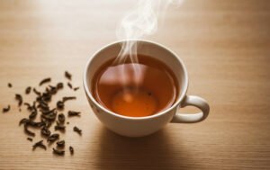 Xícara de chá quente vista de cima com folhas de chá ao redor sobre mesa de madeira clara