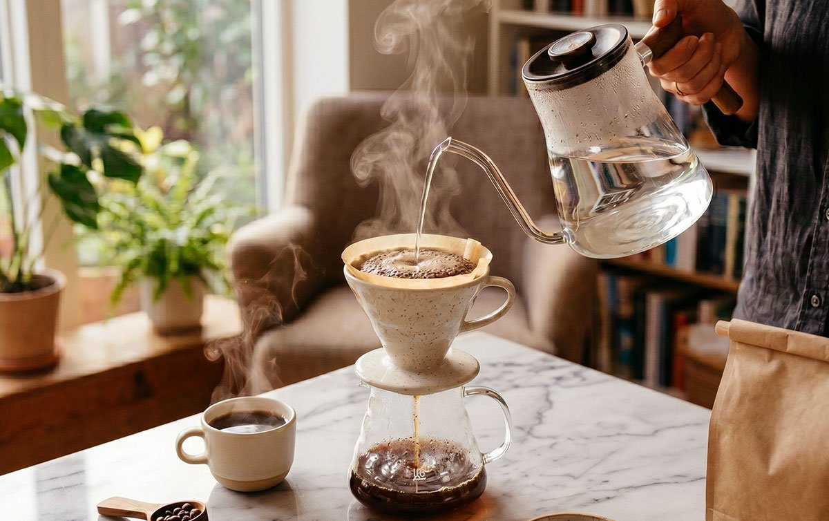 Chaleira despejando água filtrada sobre café fresco durante o preparo em ambiente aconchegante.