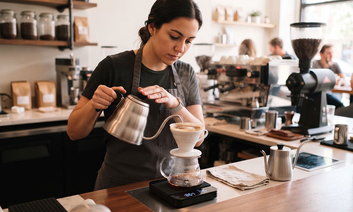 Barista preparando café filtrado com balança e moagem controlada em uma cafeteria.